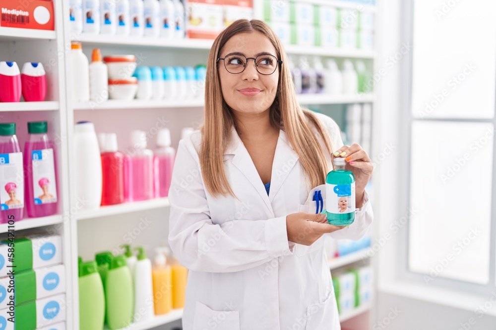 Young blonde woman working at pharmacy drugstore holding syrup smiling looking to the side and staring away thinking.