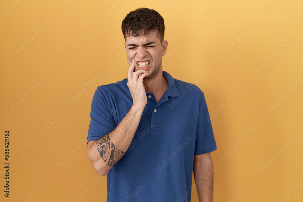 Young hispanic man standing over yellow background touching mouth with hand with painful expression because of toothache or dental illness on teeth. dentist Young hispanic man standing over yellow background touching mouth with hand with painful expression because of toothache or dental illness on teeth. dentist