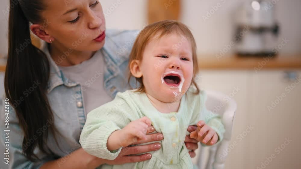 Mom holds crying baby with dirty face in kitchen at home. Baby refuses to eat porridge. Mother is kissing her crying little kid. Raising child, motherhood, parenthood love and care in family concept. Mom holds crying baby with dirty face in kitchen at home. Baby refuses to eat porridge. Mother is kissing her crying little kid. Raising child, motherhood, parenthood love and care in family concept.