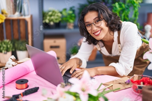 Young beautiful hispanic woman florist smiling confident using laptop at flower shop