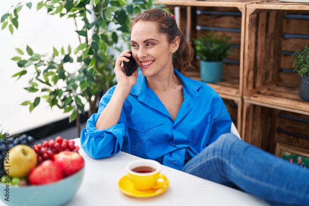 Young woman talking on smartphone drinking coffee at home