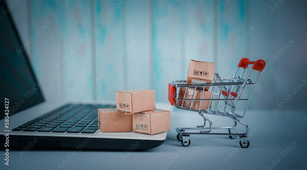 Online shopping, home delivery. Brown paper boxes in a shopping cart with laptop keyboard on table office. Easy shopping with finger tips for consumers. e-commerce and customer experience concept.