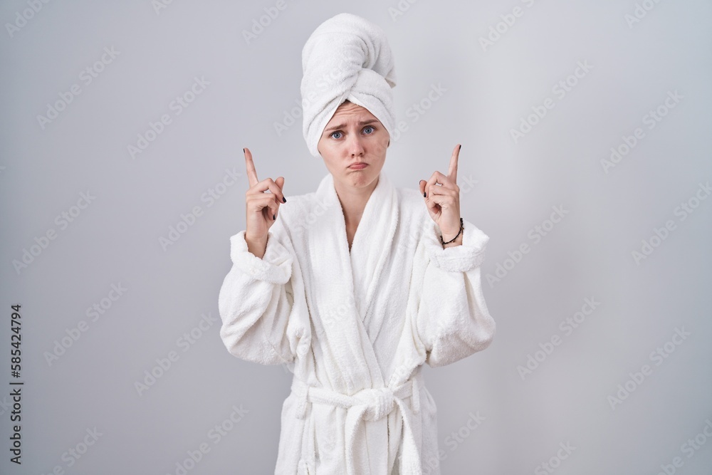 Blonde caucasian woman wearing bathrobe pointing up looking sad and upset, indicating direction with fingers, unhappy and depressed. Blonde caucasian woman wearing bathrobe pointing up looking sad and upset, indicating direction with fingers, unhappy and depressed.
