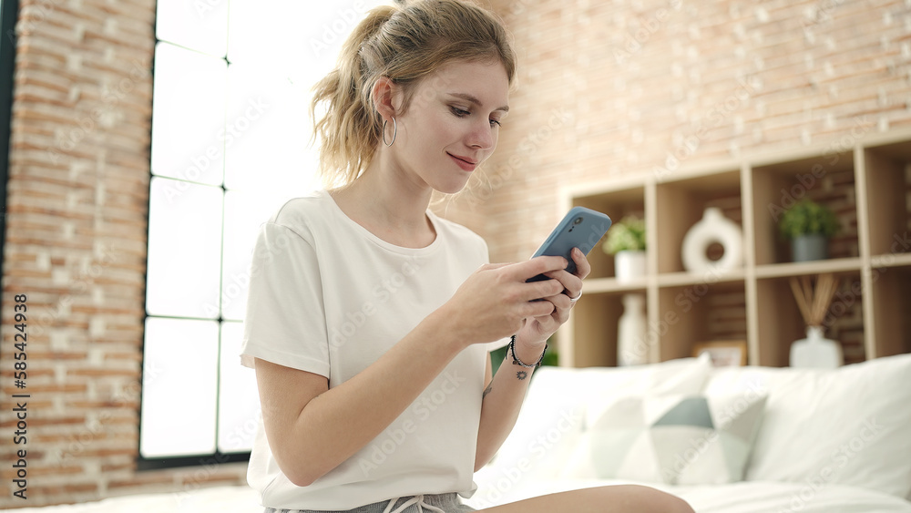 Young blonde woman using smartphone sitting on bed at bedroom Young blonde woman using smartphone sitting on bed at bedroom