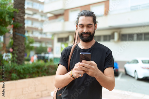 Young hispanic man musician using smartphone holding guitar case at park