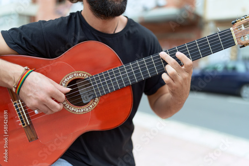 Young hispanic man musician playing classical guitar at street