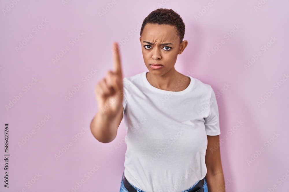 Obraz premium Beautiful african american woman standing over pink background pointing with finger up and angry expression, showing no gesture