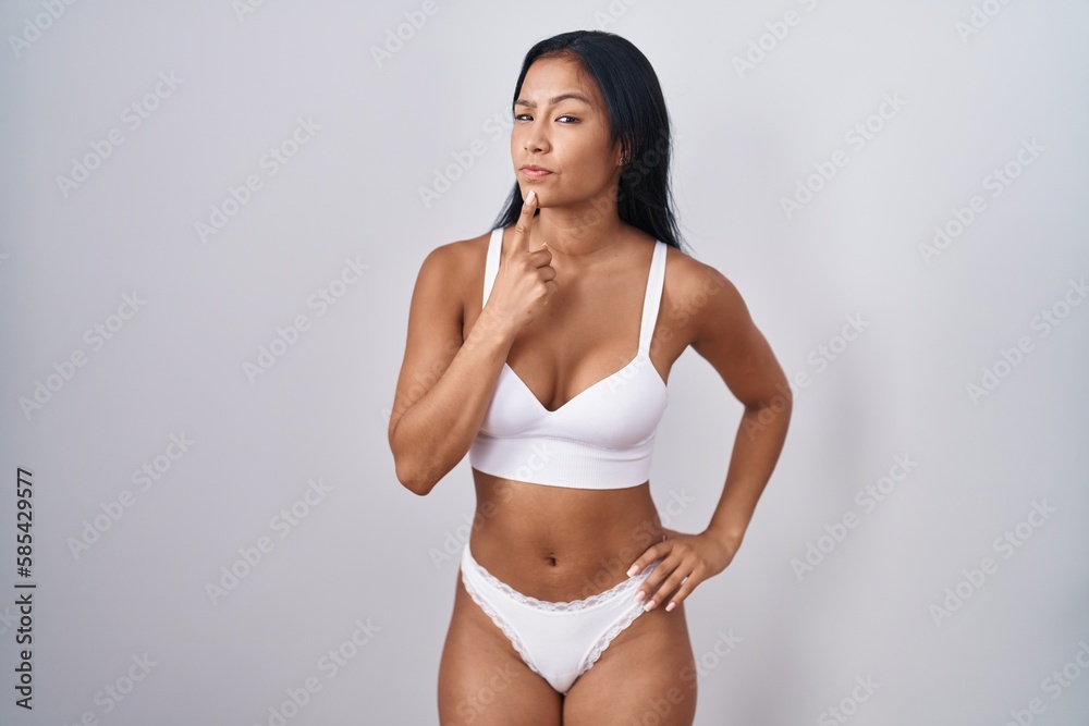 Hispanic woman wearing lingerie thinking concentrated about doubt with finger on chin and looking up wondering