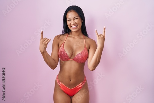 Hispanic woman wearing bikini shouting with crazy expression doing rock symbol with hands up. music star. heavy music concept.
