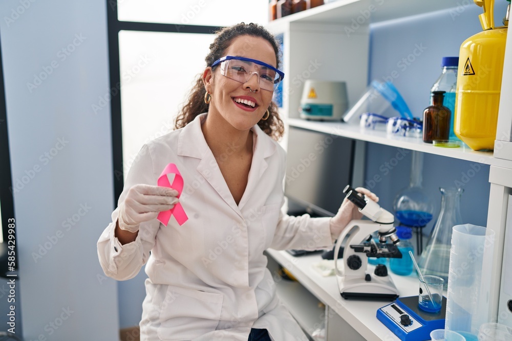 Young hispanic woman working at scientist laboratory looking for breast cancer cure smiling and laughing hard out loud because funny crazy joke. Young hispanic woman working at scientist laboratory looking for breast cancer cure smiling and laughing hard out loud because funny crazy joke.