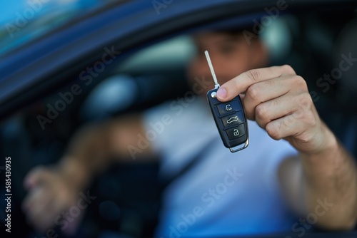 Young hispanic man smiling confident holding key of new car at street