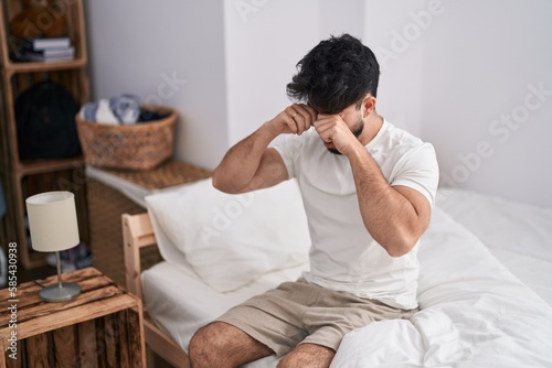 Young hispanic man tired sitting on bed at bedroom