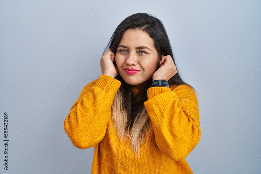 Young hispanic woman standing over isolated background covering ears with fingers with annoyed expression for the noise of loud music. deaf concept. Young hispanic woman standing over isolated background covering ears with fingers with annoyed expression for the noise of loud music. deaf concept.