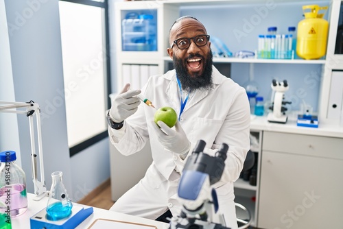 African american man working at scientist laboratory with apple celebrating crazy and amazed for success with open eyes screaming excited.