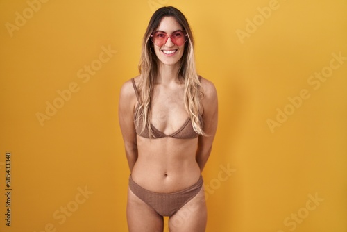 Young hispanic woman wearing bikini over yellow background with a happy and cool smile on face. lucky person.