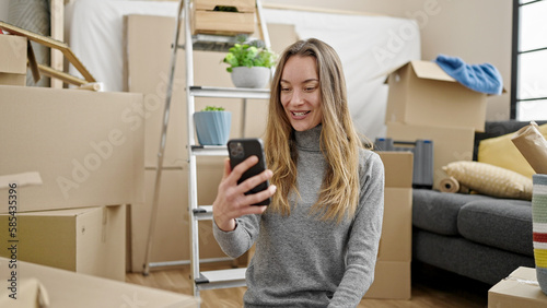 Young caucasian woman sitting on the floor using smartphone at new home