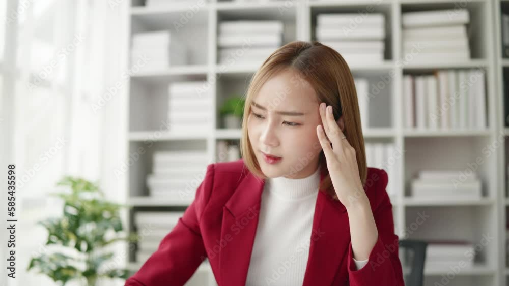 Business Woman in red suit seriously stressed working and headache due to office syndrome on laptop and paperwork in the office. Business Woman in red suit seriously stressed working and headache due to office syndrome on laptop and paperwork in the office.