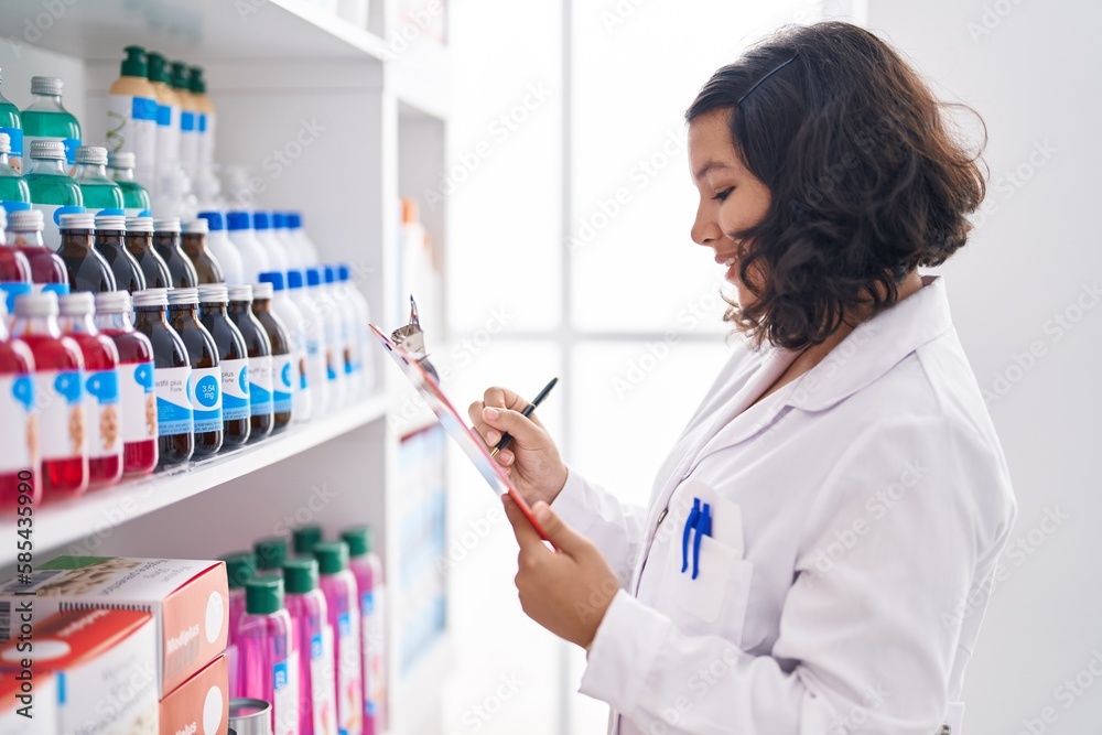 Young woman pharmacist writing on document at pharmacy