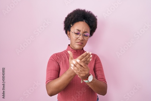 Beautiful african woman with curly hair standing over pink background suffering pain on hands and fingers, arthritis inflammation