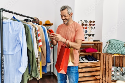 Middle age grey-haired man customer smiling confident using smartphone at clothing store
