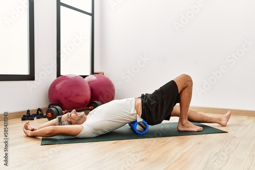 Middle age grey-haired man using foam roller stretching at sport center