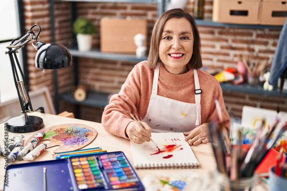 Fototapeta premium Middle age woman artist drawing on notebook at art studio