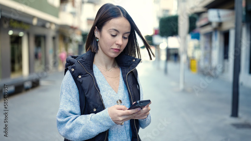 Young beautiful hispanic woman using smartphone with serious expression at street