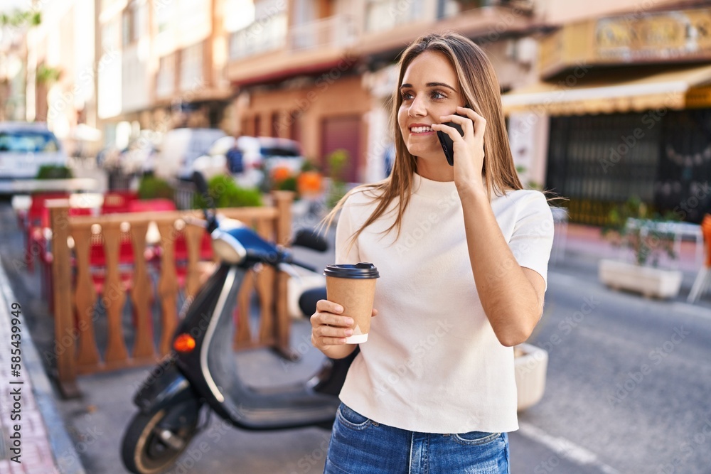 Young blonde woman talking on the smartphone and drinking coffee at street