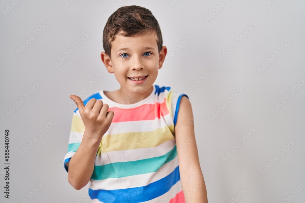 Young caucasian kid getting vaccine showing arm with band aid pointing thumb up to the side smiling happy with open mouth Young caucasian kid getting vaccine showing arm with band aid pointing thumb up to the side smiling happy with open mouth