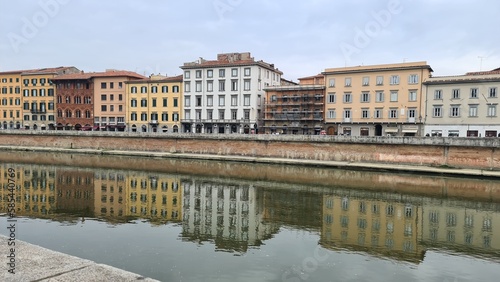 Pisa  Italy - February 25  2023  View of the medieval town of Pisa from bridge  Ponte di Mezzo  on river Arno in winter days  with grey sky in the background. Reflection of the buildings on the water.