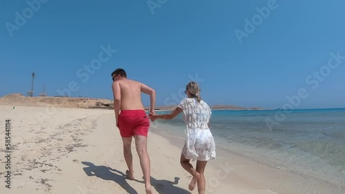 Couple running holding hands on beautiful beach wigh clear blue waters and white sand, beach of Giftun island (Paradise island) near Hurghada, Red Sea, Egypt, slow motion photo