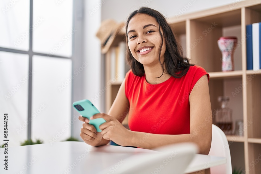 Young african american woman using smartphone sitting on table at home Young african american woman using smartphone sitting on table at home