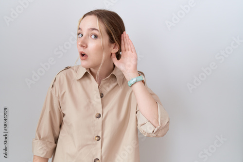 Young caucasian woman wearing casual shirt smiling with hand over ear listening an hearing to rumor or gossip. deafness concept.