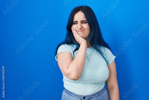 Young modern girl with blue hair standing over blue background touching mouth with hand with painful expression because of toothache or dental illness on teeth. dentist