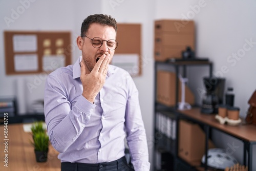 Young hispanic man at the office bored yawning tired covering mouth with hand. restless and sleepiness.