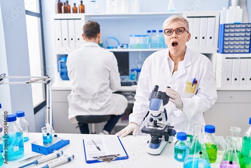 Middle age woman working at scientist laboratory scared and amazed with open mouth for surprise  disbelief face