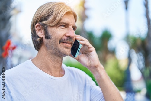 Young blond man smiling confident talking on the smartphone at park