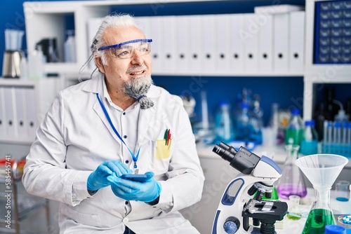 Middle age grey-haired man scientist smiling confident using smartphone at laboratory