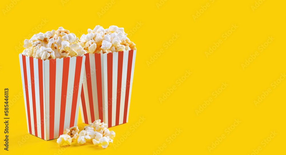 Two red white striped carton buckets with tasty cheese popcorn, isolated on yellow background. Box with scattering of popcorn grains. Fast food, movies, cinema and entertainment concept.
