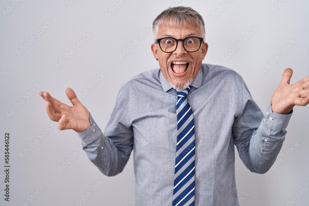 Hispanic business man with grey hair wearing glasses celebrating crazy and amazed for success with arms raised and open eyes screaming excited. winner concept Hispanic business man with grey hair wearing glasses celebrating crazy and amazed for success with arms raised and open eyes screaming excited. winner concept