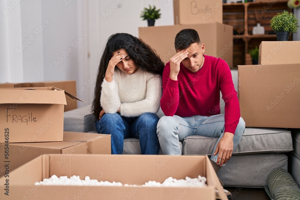 Man and woman couple with tired expression sitting on sofa at new home