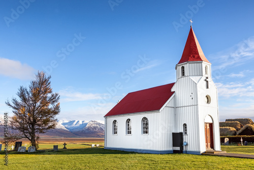 Glaumbaejarkirkja , the Glaumbaer Church, in Northern Iceland. Traditional red and white building with snow covered mountains and blue sky behind.