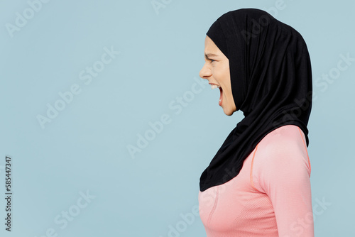 Side view young sad arabian asian muslim fitness trainer sporty woman wear pink abaya hijab spend time in home gym screa, loud isolated on plain blue background studio. Workout sport fit abs concept. photo