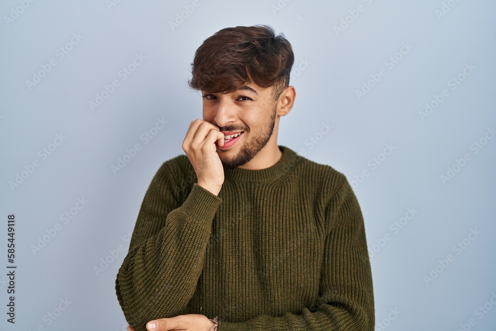 Arab man with beard standing over blue background looking stressed and nervous with hands on mouth biting nails. anxiety problem. Arab man with beard standing over blue background looking stressed and nervous with hands on mouth biting nails. anxiety problem.