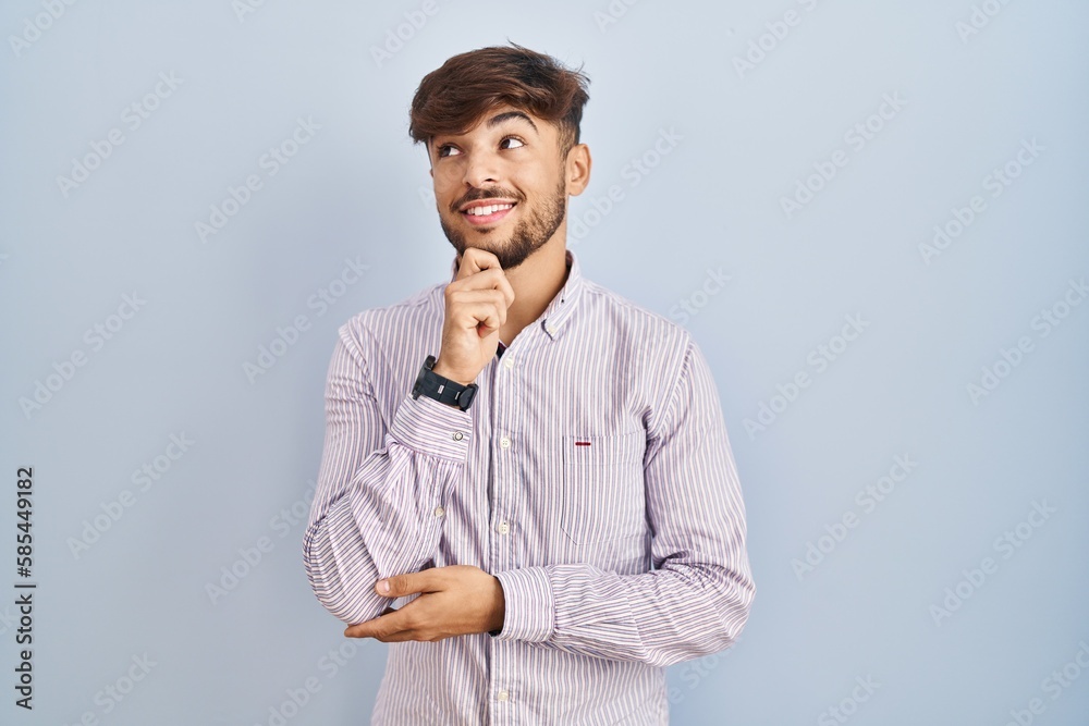 Arab man with beard standing over blue background with hand on chin thinking about question, pensive expression. smiling and thoughtful face. doubt concept. Arab man with beard standing over blue background with hand on chin thinking about question, pensive expression. smiling and thoughtful face. doubt concept.