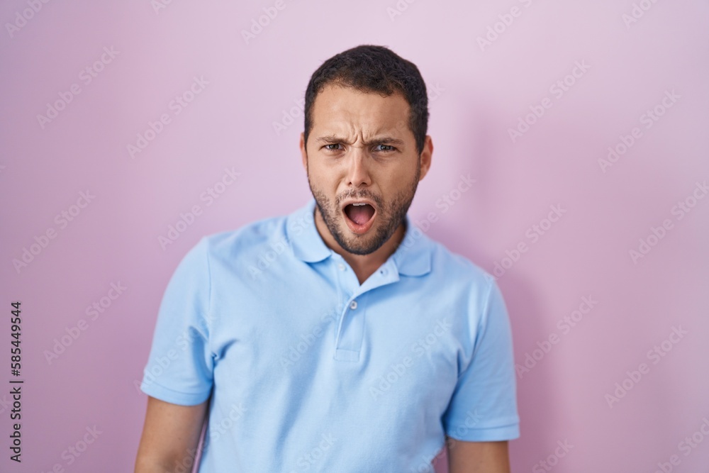 Hispanic man standing over pink background in shock face, looking skeptical and sarcastic, surprised with open mouth Hispanic man standing over pink background in shock face, looking skeptical and sarcastic, surprised with open mouth