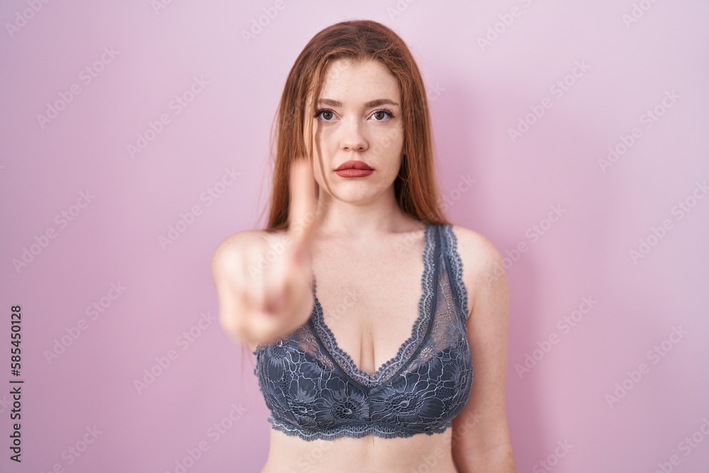 Redhead woman wearing lingerie over pink background pointing with finger up and angry expression, showing no gesture Redhead woman wearing lingerie over pink background pointing with finger up and angry expression, showing no gesture