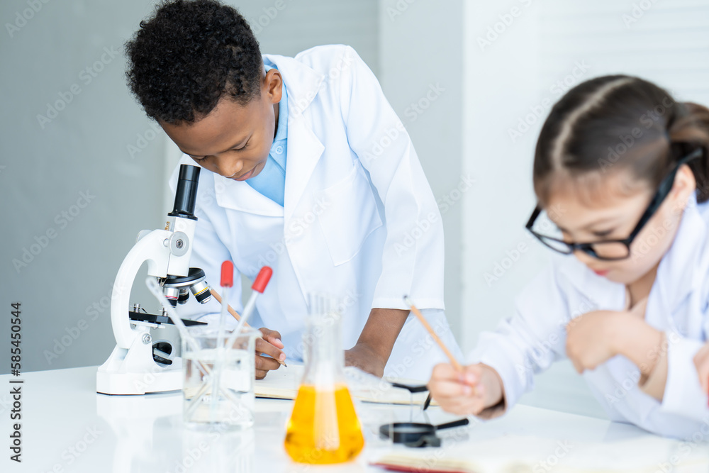 A young African boy and a little Asian girl in white lab coat help each other for experiment. A boy using microscope and recording information. A girl holding pencil in hand and thinking something. A young African boy and a little Asian girl in white lab coat help each other for experiment. A boy using microscope and recording information. A girl holding pencil in hand and thinking something.