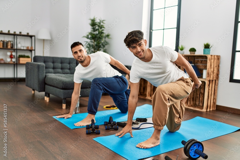 Two hispanic men couple smiling confident stretching at home