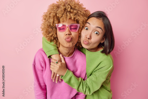Foto Photo of two female best friends embrace and pout lips stands closely to each other dressed in casual jumpers isolated over pink studio background have good relationships